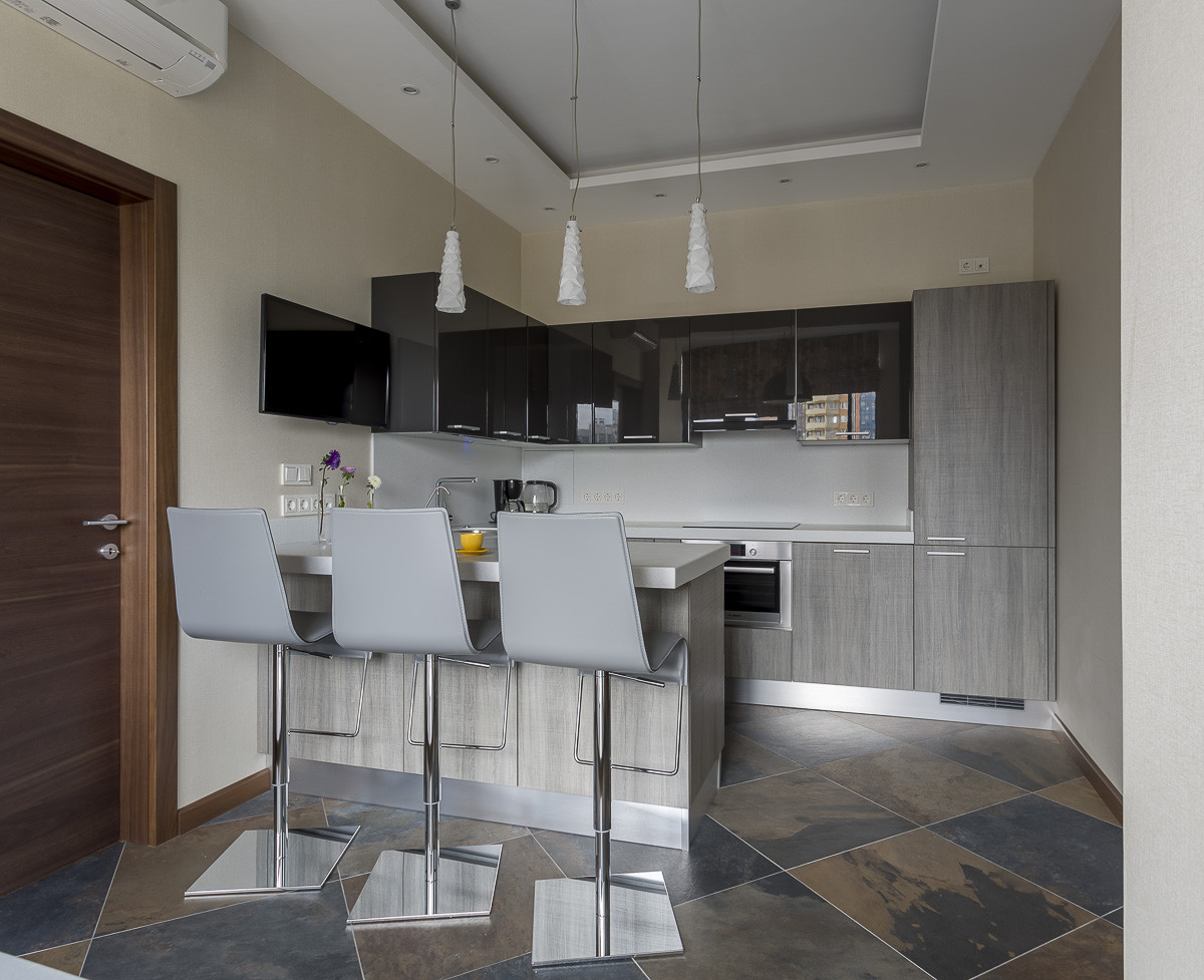 Кухонная мебель выполнена на контрасте текстур — глянца верхних полок и фактурного дерева внизу. Столешница из искусственного камня объединяет П-образную кухню в единую композицию и служит барной стойкой.